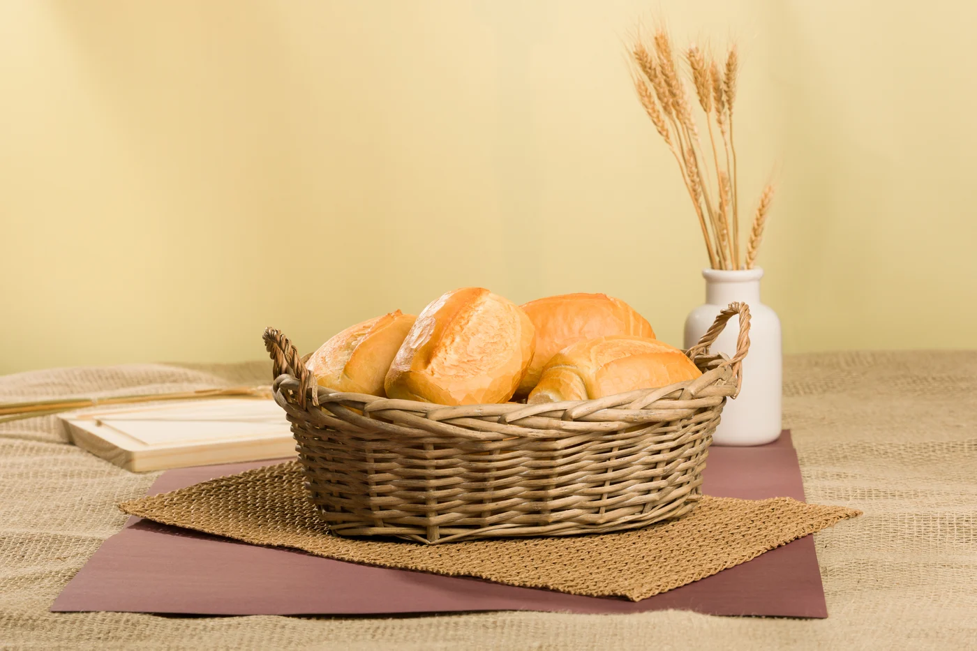 Pães franceses em uma cesta com trigo e madeira na composição